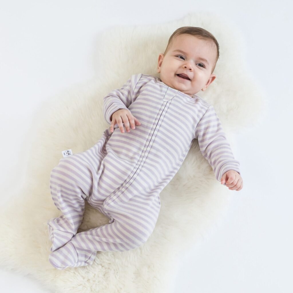 Happy baby lying on a rug wearing lilac striped footie pajamas