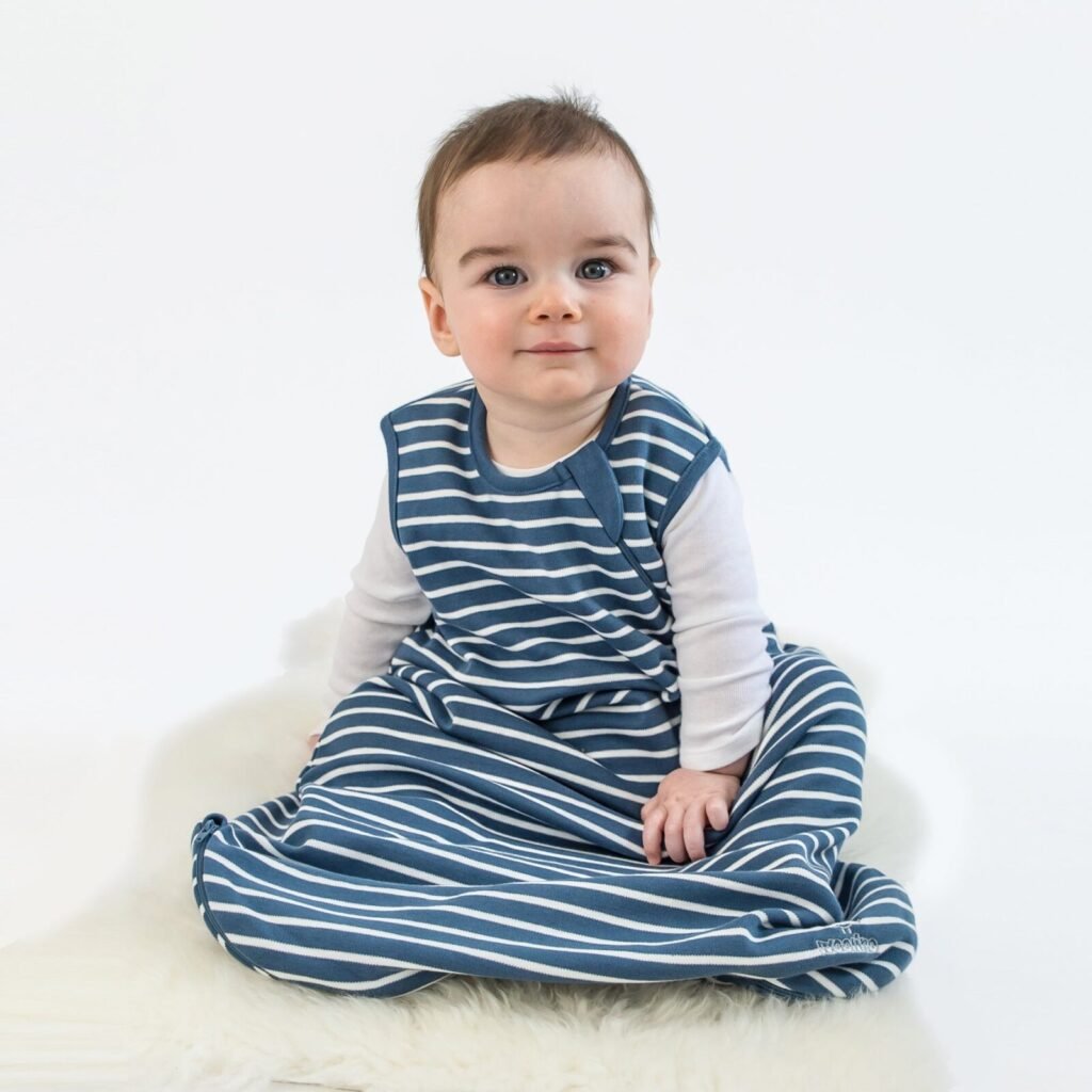 Baby sitting on a lambskin rug wearing a navy striped sleep bag