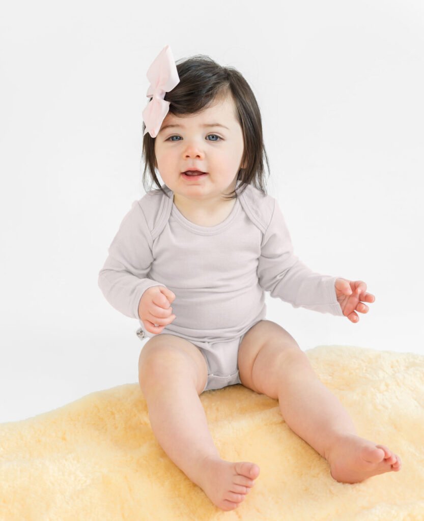 Baby sitting on a lambskin rug wearing a soft wool bodysuit